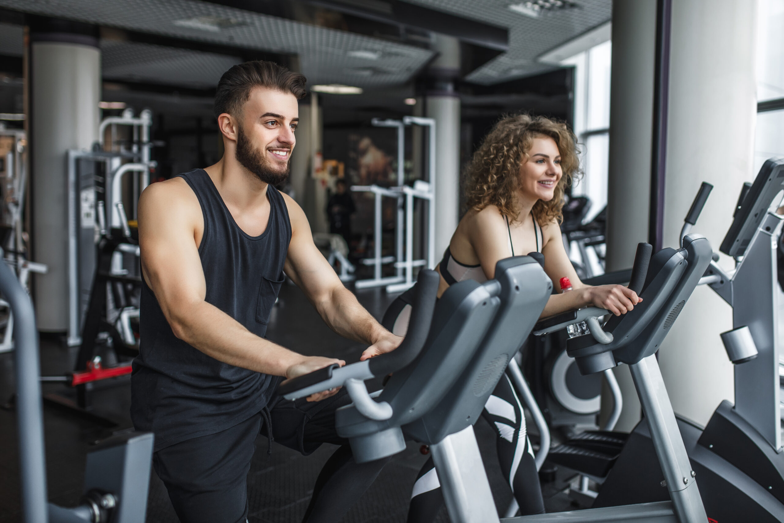 Attractive young woman and her trainer running on treadmill in g